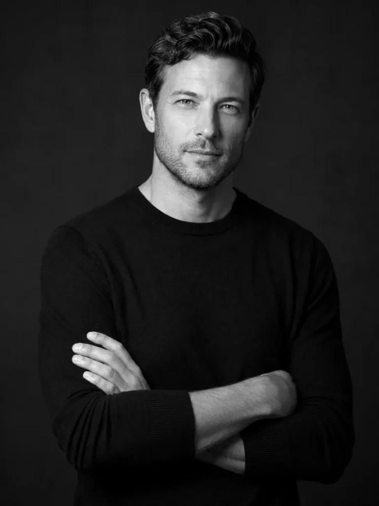 High-contrast black-and-white founder portrait of a man against a charcoal studio background with soft side lighting.