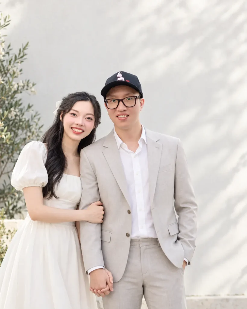 Gemini Couple Photo Prompts example of a couple standing against a bright neutral outdoor wall in coordinated semi-formal clothing with hands loosely held and open space around them