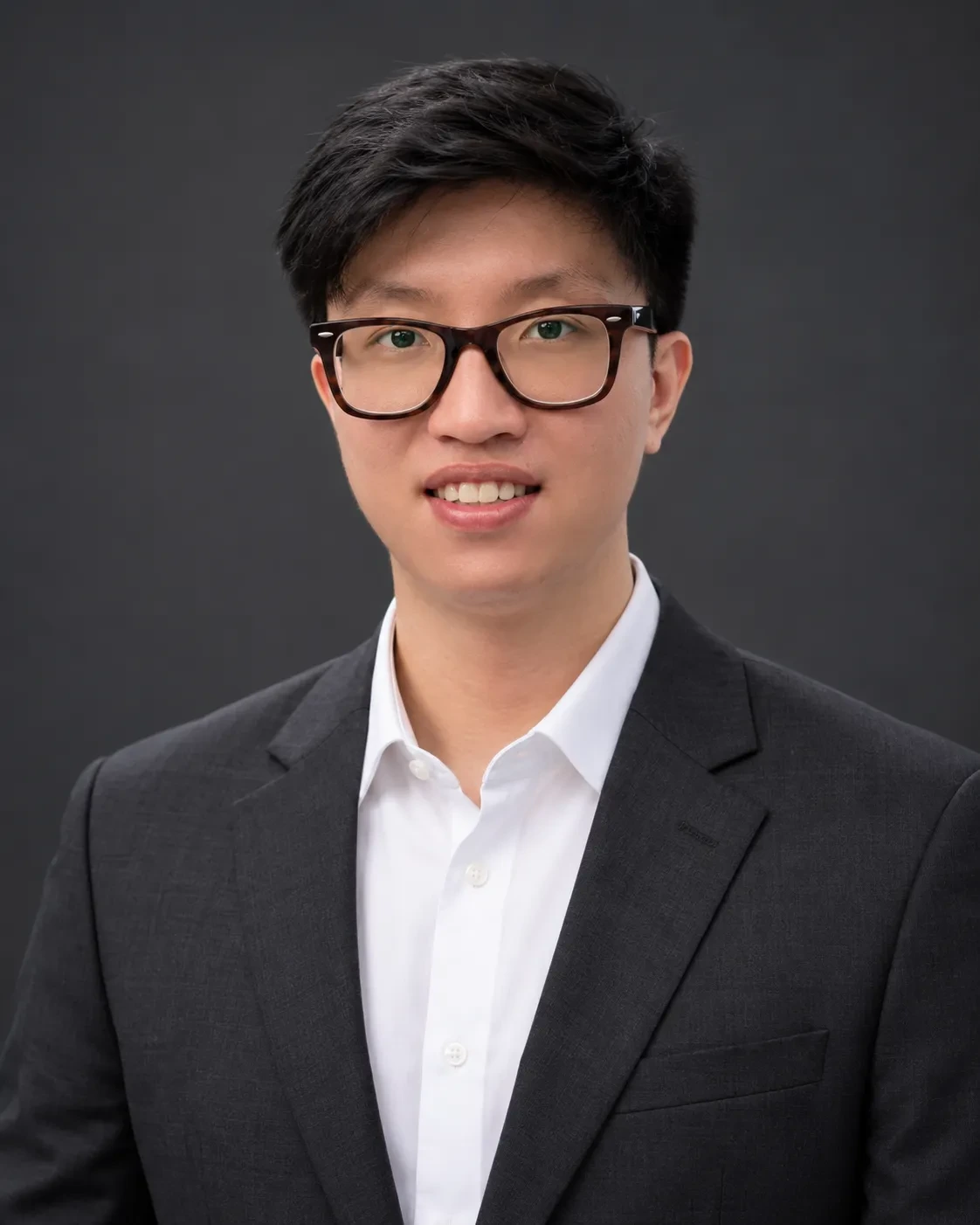 Chest-up headshot of a man in glasses wearing a charcoal suit jacket and white shirt on a dark gray backdrop