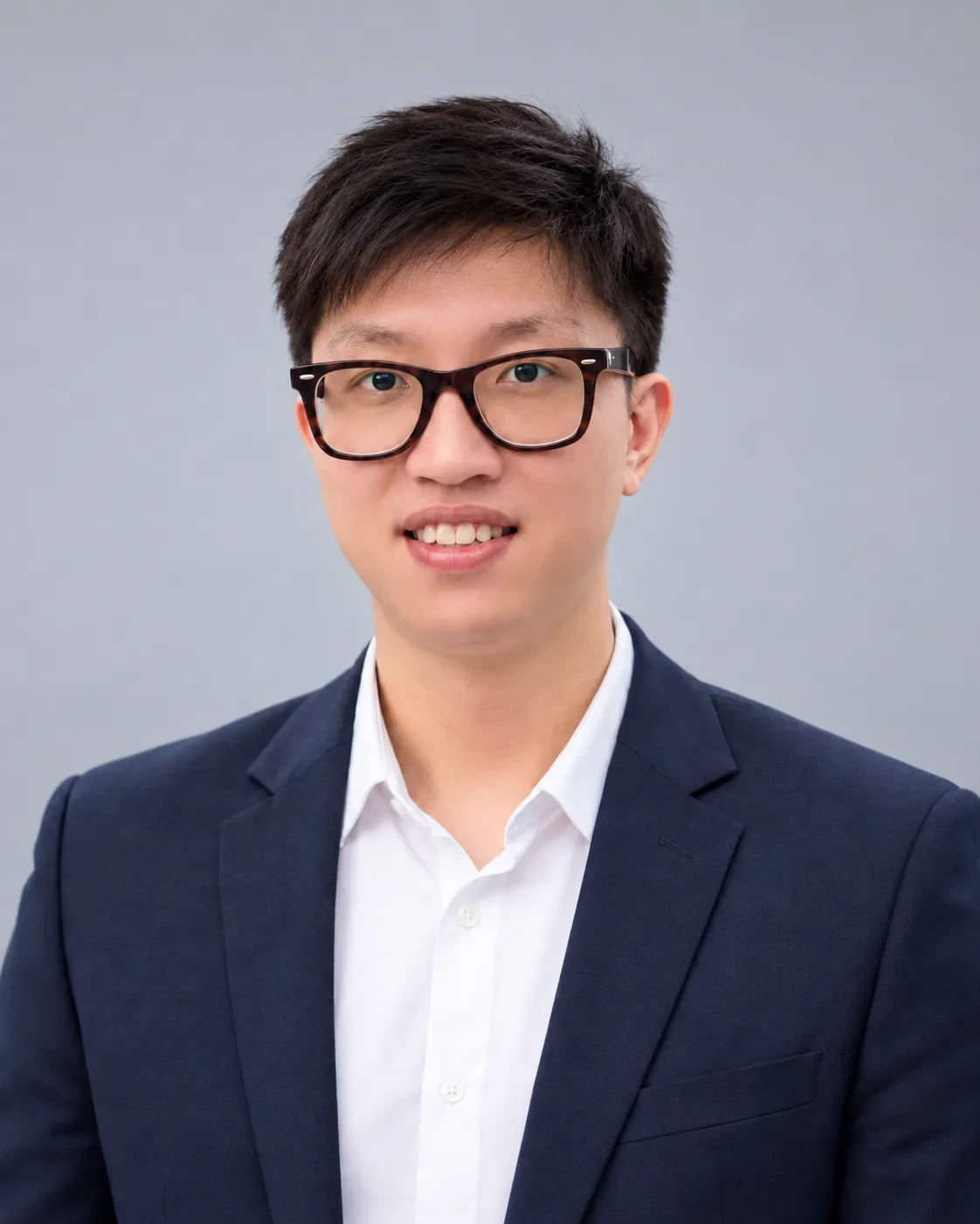 Chest-up headshot of a man in glasses wearing a navy blazer and white shirt on a plain light gray studio backdrop